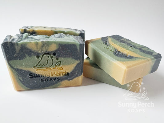Four soap bars with a visible brand logo on a white background. Soap color is swirls of green, dark gray and yellow in color.