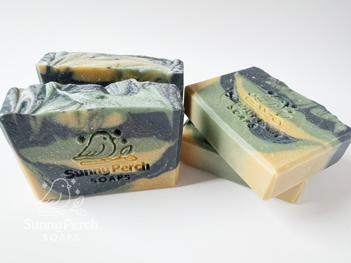 Four soap bars with a visible brand logo on a white background. Soap color is swirls of green, dark gray and yellow in color.